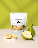 A package of freeze-dried pear slices for pets, with a few slices visible outside the package, alongside a whole pear.